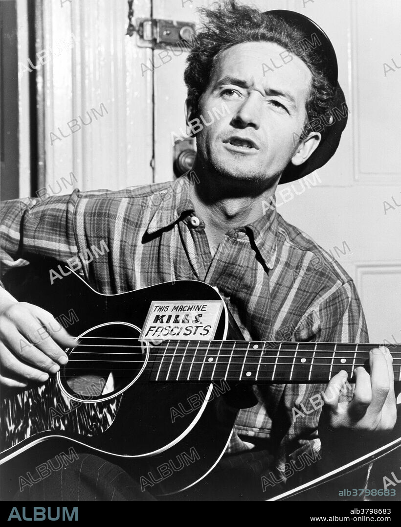 Woodrow Wilson "Woody" Guthrie (July 14, 1912 - October 3, 1967) was an American singer-songwriter and musician whose musical legacy includes hundreds of political, traditional and children's songs, ballads and improvised works. He frequently performed with the slogan This machine kills fascists displayed on his guitar. His best-known song is "This Land Is Your Land." Many of his songs are about his experiences in the Dust Bowl era during the Great Depression when Guthrie traveled with displaced farmers from Oklahoma to California and learned their traditional folk and blues songs, earning him the nickname the "Dust Bowl Troubadour." Throughout his life Guthrie was associated with United States Communist groups, though he was seemingly not a member of any. Guthrie was married three times and fathered eight children, including American folk musician Arlo Guthrie. He died in 1967, at the age of 55, from complications of Huntington's disease, a progressive genetic neurological disorder. During his later years, in spite of his illness, Guthrie served as a figurehead in the folk movement, providing inspiration to a generation of new folk musicians. Photographed by Al Aumuller for New York World Telegram & Sun, dated March 8, 1943.