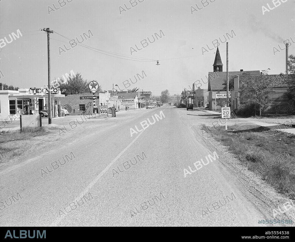 DOROTHEA LANGE. Main street of Nyssa, Oregon, on Saturday afternoon. [Signs: 'Texaco; Don't Hibernate - Insulate!; Blacksmithing; Coffee Shop & Tavern; Gas; Garage, Welding & Repairing, Body & Fender Repairing, Auto Painting; Wilson Bros Dry Goods; Main's Cleaners; Drugs Fountain; Atkeson's Clothing - Women's Apparel; Real Estate; Speed 20 Miles'].