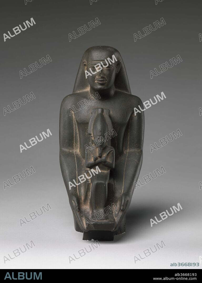 Padiamunrenebwaset, son of Irethoreru, holding a seated statue of Osiris. Dimensions: H. 22.5 cm (8 7/8 in.); W. 10.4 cm (4 1/8 in.); D. 12.2 cm (4 13/16 in.). Date: 4th century B.C., late.
This statue depicts the priest Padiamunrenebwaset. Padiamunrenebwaset has balanced, slightly smiiling features with very long narrow eyes. The priest's fingertips curl very slightly to hold a seated figure of Osiris.
The lower part of the statue is located in the Egyptian Museum, Cairo, and was discovered in the Karnak Cachette and matched by Egyptologists. Together the two fragments depict the individual in a long kilt with a projecting front; the lower part also reveals that the statue of Osiris is actually seated on a tall pillar that merges invisibly with the skirt in the upper part of the statue, but appears beneath the skirt next to Padiamunnebrewaset's feet. The inscriptions on the statue's skirt reveal that Padiamunrenebwaset was a prophet of Khonsu in Thebes Neferhotep, and state that he served for 80 years, probably an ideal span as it is sometimes claimed by other officials. The statue's appearance reveals this period's a fondness for the style of features seen in the earlier Saite Period; however, the version of the formula on the backpillar and the inscriptions that cover the skirt make it clear that this statue, and another one of the owner's son, actually date to the beginning of the Ptolemaic Period, roughly 300 years later.