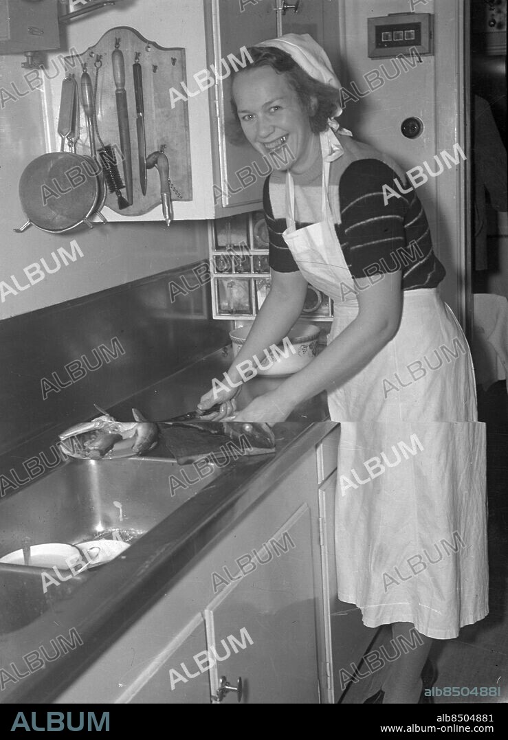 Göteborg 1943-11-19 - Kvinna i kök rensar fisk - det kan vara ett hembiträde vi ser - bakom henne på väggen finns signalanordningen som förr användes i "finare" hem. *** Local Caption *** GT Låda Krep 2011-05. KAMERAREPORTAGE.