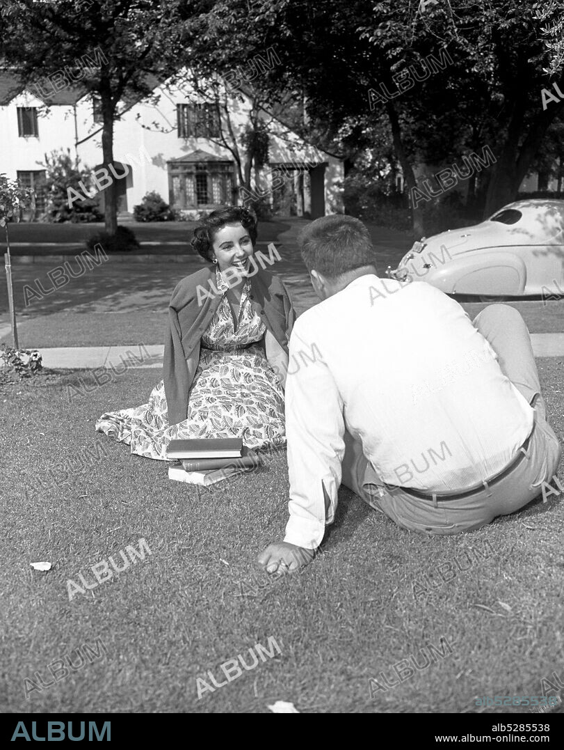 ELIZABETH TAYLOR. 1947, Hollywood, California, USA: ELIZABETH (LIZ) TAYLOR in printed dress and cardigan, with books and a male friend in her garden at home in Hollywood. (Credit Image: © Frank Worth/ZUMA Wire).