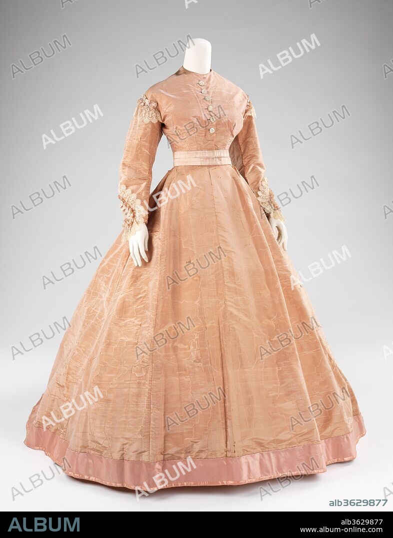Evening dress. Culture: American. Designer: Mme. Olympe (American, born France, 1830). Date: ca. 1865.
This is one of two extant dresses bearing a Mme. Olympe label.  Olympe Boisse was a French-born New Orleans dressmaker who regularly traveled to Paris to keep abreast of trend-setting French fashions of the time.such as those by Charles Frederick Worth and Emile Pingat.  Mme. Olympe, as she was professionally known, initially was an importer of French goods but in time designed and sold her own garments. Her claim to fame is that, considering the date of this dress, she was one of the first, if not the first, American dressmakers to label her gowns, a practice intiated by Worth et Bobergh in the early 1860s. 
The Worth influence in this dress is readily seen in comparison to the Worth et  Bobergh gown 2009.300.1372a-d in its silhouette and cut. The simple styling makes the beauty and femininity of the textile truly shine.  
The female silhouette of the middle of the 19th century consisted of a fitted corseted bodice and wide full skirts.  The conical skirts developed between the 1830s, when the high waist of the Empire silhouette was lowered and the skirts became more bell shaped, to the late 1860s, when the fullness of the skirts was pulled to the back and the bustle developed.  The flared skirts of the period gradually increased in size throughout and were supported by a number of methods.  Originally support came from multiple layers of petticoats which, due to weight and discomfort, were supplanted by underskirts comprised of graduated hoops made from materials such as baleen, cane and metal.  The fashions during this time allowed the textiles to stand out because of the vast surface areas of the skirt and a relatively minimal amount of excess trim.