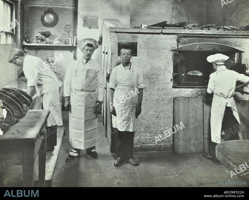 Boys making bread at Upton House Truant School, Hackney, London, 1908. Scene in the bakery; one boy gets a loaf of bread out of the oven, another poses with the instructor while a third attends to the dough.