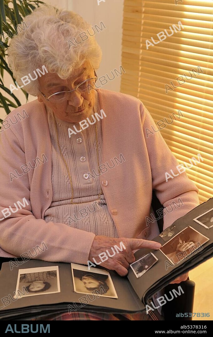 Elderly woman looking through photo album filled with old family portraits