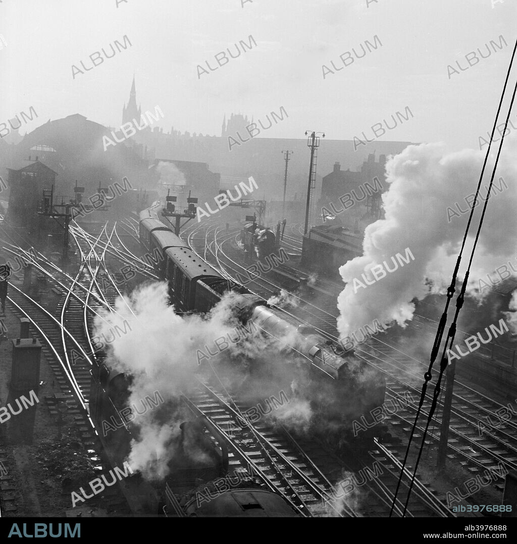 Steam trains at King's Cross, London, 1946-1969. An elevated viewpoint of the railway track to the north of the station, showing a steam engine and carriages passing another.