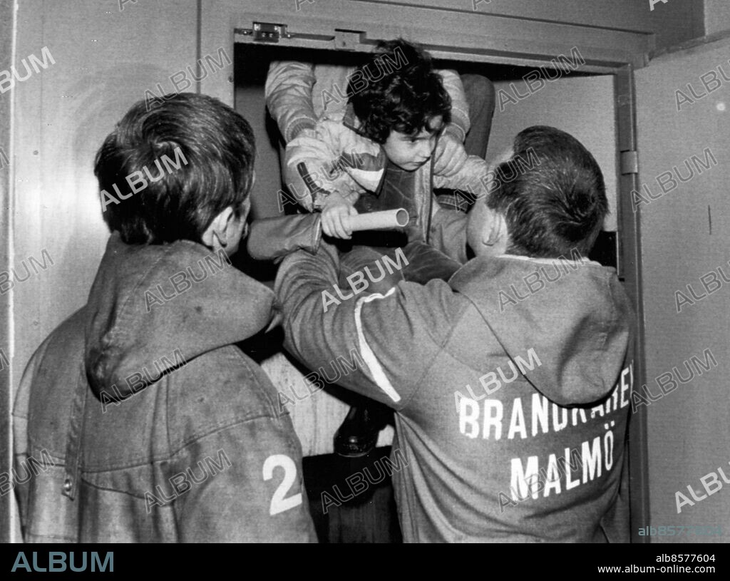 ARKIV 19831227. Fyraårige Göknan Güul lyfts ut ur hissen av brandmännen Bertil Ransbäck (t.v.) och Roland Holmgren efter att ha suttit fast i närmare en timme och fyrtiofem minuter i ett bostadshus i Malmö 27:e december 1983. Hisstoppet orsakades av ett strömavbrott som lamslog stora delar av Sverige då en frånskiljare gick sönder i ställverket på transformatorstationen i Hamra utanför Enköping.. Foto: Ulf Ryd / XP / SCANPIX / Kod: 38. **AFTONBLADET OUT**.