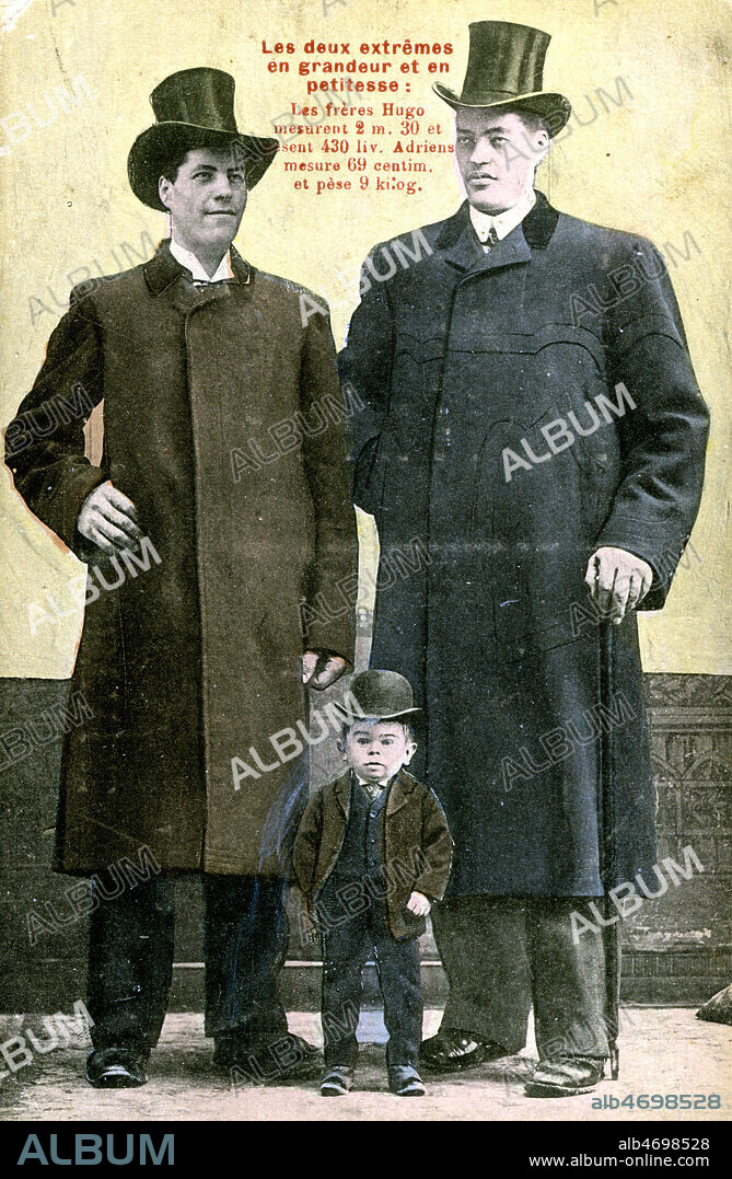 Les Freres Hugo avec un nain. Les freres Hugo presentent un cas de gigantisme unique au monde. Ils sont nes a St Martin Vesubie dans une petite maison isolee sur la montagne. Baptiste l'aine mesure 2.30 et pese 430 livres. Antoine son frere est ne en 1889,il mesure 2.25 et pese 300 livres, sa taille s'accroit actuellement de 10 centimetres par an. D'apres la faculte de medecine, Antoine Hugo grandira encore plusieurs annees. Les freres Hugo detiennent le record de tous les geants et offrent 1000 francs a leur rival. Carte postale vers 1910. Credit : Jean Vigne/KHARBINE-TAPABOR.
