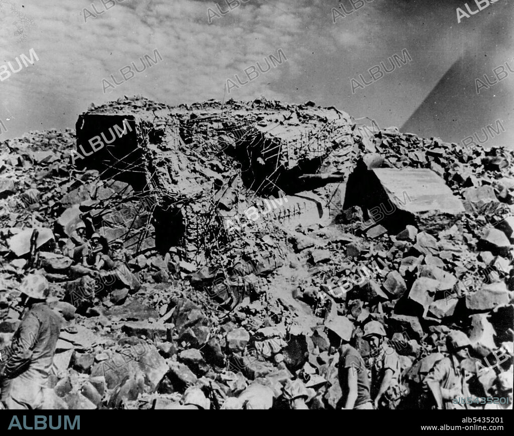 Eight-Foot Thick Walls On Jap Pill Box -- Located on Mt. Suribachi on Iwo Jima took a dead hit from one of the Navy's big guns. The terrain of broken lava rock makes it almost impossible to see the 14 Marines and Coast Guardsmen taking a breather near by. March 19, 1945. (Photo by Official U.S. Coast Guard Photo).