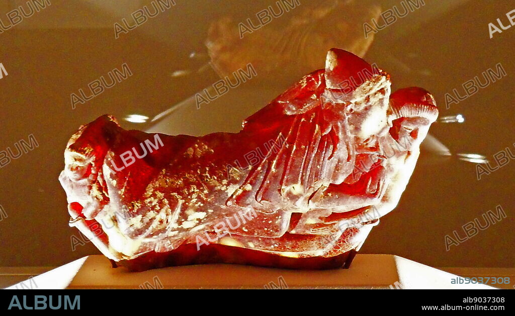 Carved amber bow of Fibula. Etruscan, circa 500 BC. The carving shows a couple reclining on a couch, with an attendant and a bird. On of the most complex carved ambers surviving from ancient Italy.