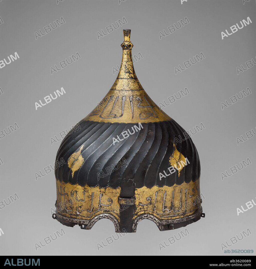 Turban Helmet. Culture: Turkish, possibly Istanbul, in the style of Turkman armor. Dimensions: H. 11 7/8 in. (30.2 cm); Diam. 9 in. (22.9 cm); Wt. 3 lb. 12.9 oz. (1272.9 g). Date: late 15th-16th century.
Helmets of this type are usually called turban helmets becuase of their large bulbous shape and the flutings that imitate the folds of a turban. Because certain dervish groups wore turbans wound with a prescribed number of folds to represent an important mystical number, it is likely that turban helmets were regarded not merely as armor but also as a kind of religious insignia, their very shape marking the wearer as a fighter in a Holy War.
Turban helmets, together with mail-and-plate armor of matching decoration, were intended for the heavy cavalry and are recorded as early as the fourteenth century. The examples exhibited here appear to have belonged to the dynasty of Ak-Koyunlu (White Sheep Turkoman) that ruled northwestern Iran and Anatolia in the fifteenth century. The inscriptions, damascened with gold and silver, glorify temporal rulers, wish the owner well, or give advice on how to attain virtue.