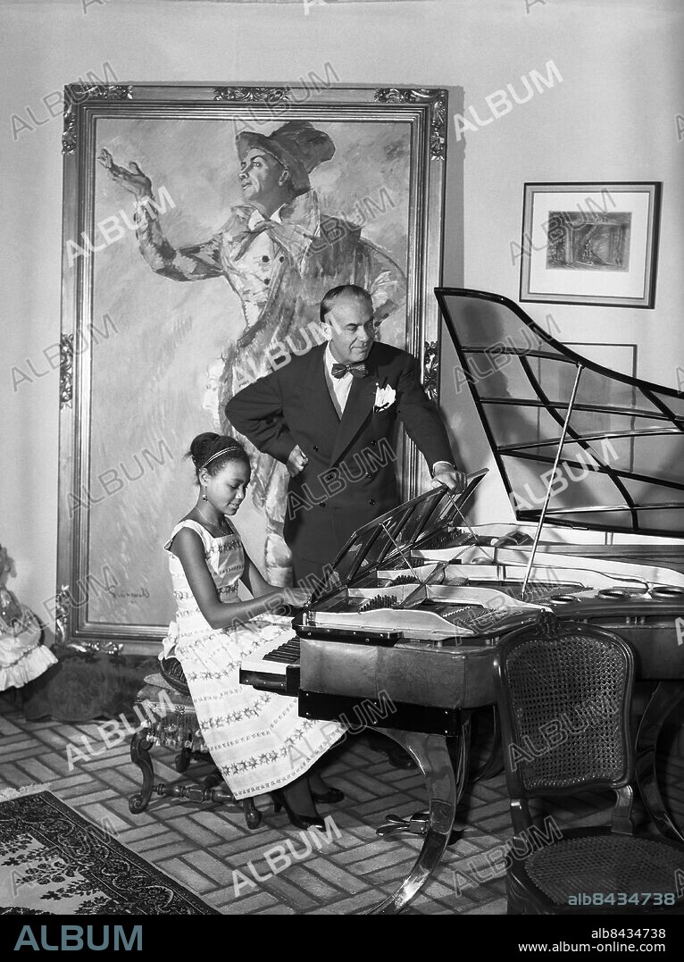 STOCKHOLM 1956-09-01. Karl Gerhard med adoptivdottern Fatima Gerhard tillsammans vid flygeln hemma i villan i Saltsjöbaden. Foto: TT Historical / kod 1900.