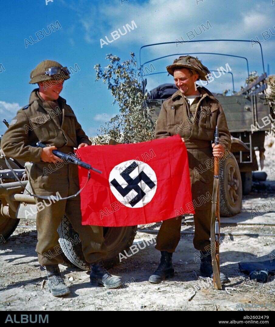 Two canadian soldiers hold a Nazi flag which they captured in a French quarry, just south of Hautmesnil. Dated 1944.