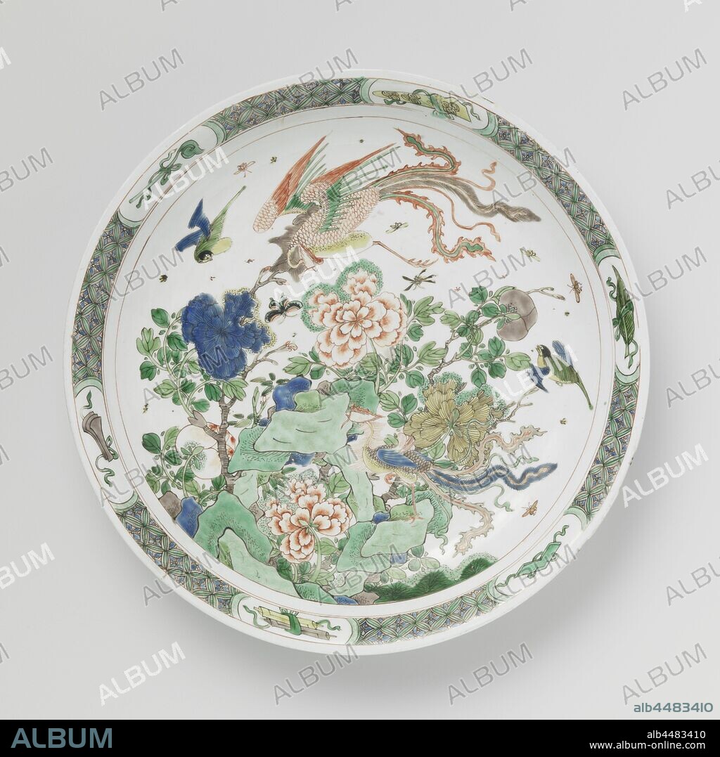 Saucer-dish with rocks, flowers and feng huangs, Saucer with round, spreading porcelain wall, painted in underglaze blue and above the glaze blue, red, green, yellow, eggplant and black. On the flat rocks with flowering peony branches and two feng huangs, other birds and insects, the border with geometric pattern interspersed with lucky symbols (castanets, scepter, book scrolls, music stone, artemisia leaf) in cartouches. The bottom with three flower sprays. Marked with a seal mark in a double circle. Four chips in the edge. Famille verte., anonymous, China, c. 1700 - c. 1724, Qing-dynasty (1644-1912) / Kangxi-period (1662-1722) / Yongzheng-period (1723-1735), porcelain (material), glaze, cobalt (mineral), vitrification, h 5.5 cm d 35.5 cm d 20.8 cm.