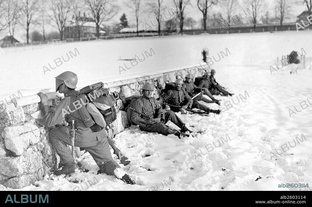 Image shows a Swiss soldier in the snow peeking over a wall, while his fellow soldiers take cover. Dated around 1917.