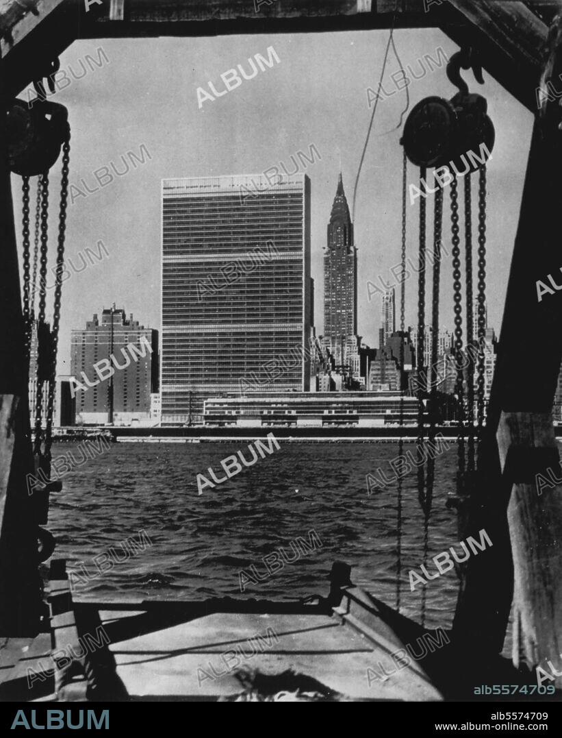 The U.N. Scene -- The new United Nations buildings in Manhattan are framed by a pier loading platform in this view made across,the East river. The tall rectangular building is the U.N. Secretariat, or office building now in use. The long, low building nearer the river front is the General Assembly building now under construction. The Chrysler building is the skyscraper in the background at right of the Secretariat. March 11, 1951. (Photo by AP Wirephoto).