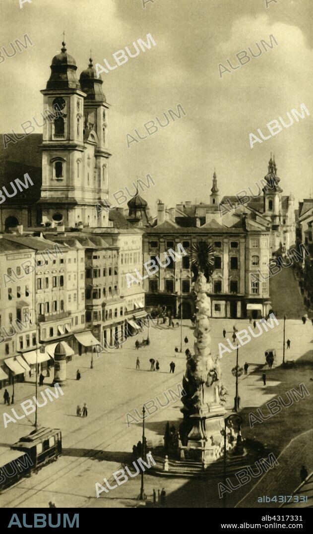 Main Square, Linz, Upper Austria, c1935. View of the Hauptplatz in the city of Linz, with the Old Cathedral (Alte Dom) on the left, built 1669-1683 in Baroque style. In the foreground is the Dreifaltigkeitssäule, (Holy Trinity column), a Pestsäule ('plague column'), erected in 1723 in remembrance of victims of the plague. From "Österreich - Land Und Volk", (Austria, Land and People). [R. Lechner (Wilhelm Müller), Vienna, c1935].