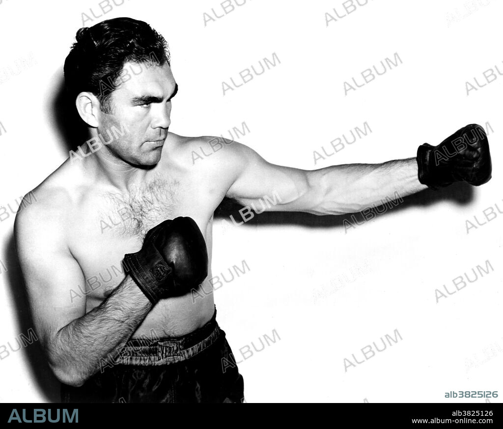 Schmeling wearing boxing trunks and gloves, 1938. Maximillian Adolph Otto Siegfried "Max" Schmeling (September 28, 1905 - February 2, 2005) was a German boxer. Starting his professional career in 1924, Schmeling came to the United States in 1928. He became the first to win the heavyweight championship by disqualification in 1930, after opponent Jack Sharkey knocked him down with a low blow in the 4th round. He retained his crown successfully in 1931 by a TKO victory over Young Stribling. A rematch in 1932 with Sharkey saw the American gaining the title from Schmeling by a controversial 15 round split decision. In 1933, Schmeling lost to Max Baer by a 10th round TKO. The loss left people believing that he was past his prime.  In 1936, he knocked out American rising star Joe Louis, placing him as the number one contender for Jim Braddock's title, but Louis got the fight and knocked Braddock out to win the championship in 1937. Schmeling finally got a chance to regain his title in 1938, but Louis knocked him out in one round. During WWII, Schmeling served with the German Air Force (Luftwaffe) as an elite paratrooper. After the war, he mounted a comeback, but retired permanently in 1948. He  died in 2005 at the age of 99. In 2003, he was ranked 55 on The Ring magazine's list of 100 greatest punchers of all time. Photographed for the New York World-Telegram and the Sun Newspaper by William C. Greene, 1938.