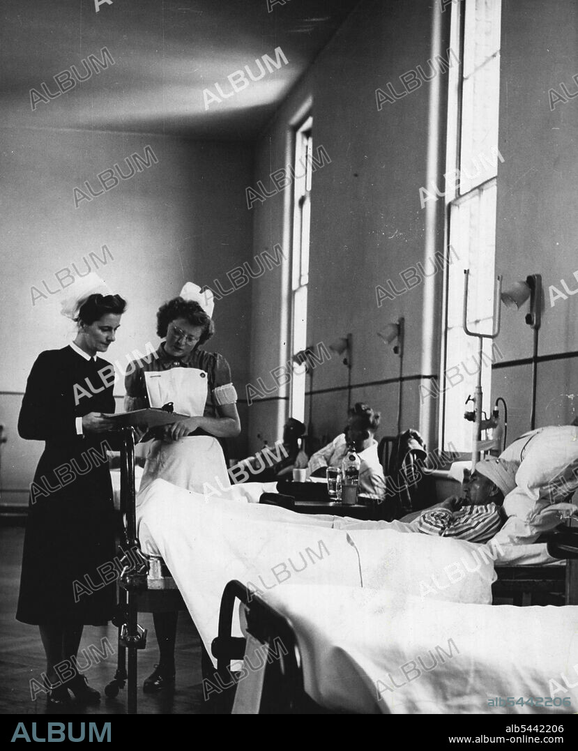 Life And Work Of A Hospital Matron -- In the absence of the Ward Sister, the Charge Nurse is head of the Nursing team in the ward. Here she is showing the Matron the nursing record of a patient who has had a Brian operation. November 22, 1950. (Photo by Tom L. Blau, Camera Press).