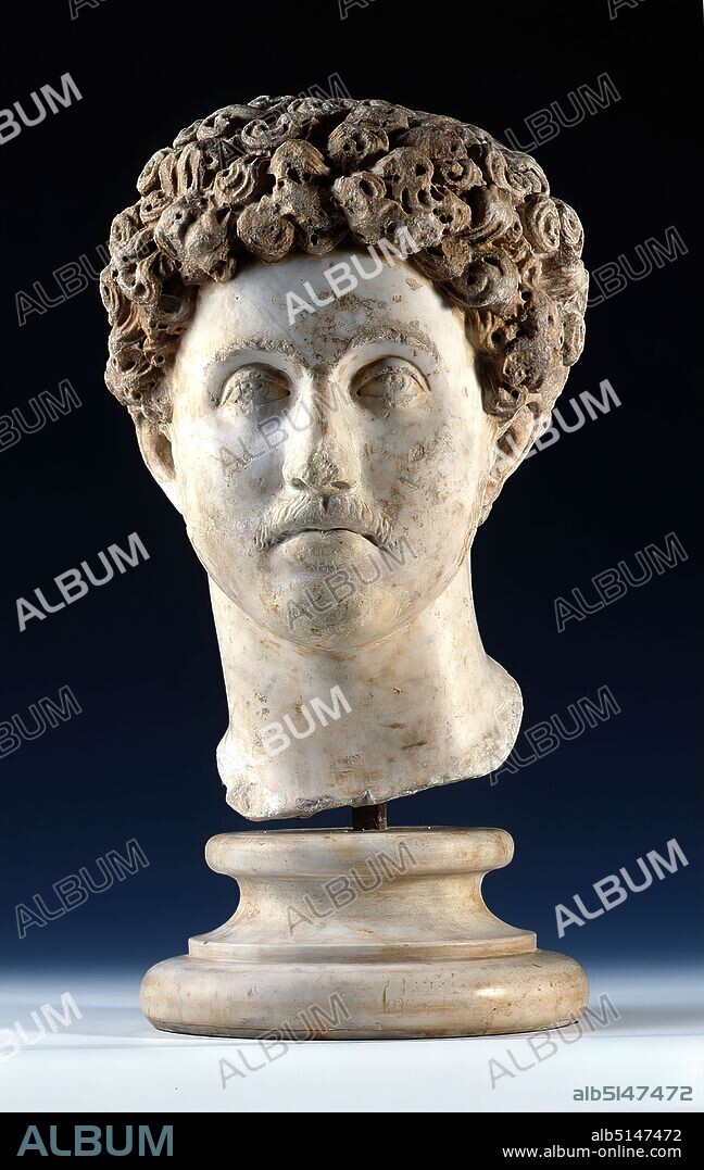 Portrait of Emperor Marcus Aurelius, marble, chiseled, drilled, beaten, marble, Total: Height: 43 cm (without base); Width: 31 cm; Depth: 31,5, Sculptures, Portrait, Emperor, Ruler's Portrait, State Portrait, Historical Person, Hairstyle Fashion, Hair Fashion, Roman Empire, Emperor Marcus Aurelius, Middle Imperial Period, The larger-than-life portrait shows a young man whose facial features are calm and unemotional The main hair is curled profusely and is a clear contrast to the beginning beard growth that can be seen on the upper lip and cheeks. Comparison with other surviving portraits - including those on coins that can be dated well - allows the sitter to be identified as the youthful Marcus Aurelius. This is the so-called 2nd type of portrait, which shows the young prince. The larger-than-life-size portrait was an insert head that once belonged to a statue about 3 m high, which is lost today. Marcus Aurelius Antoninus - so his full name - was born in Rome in 121 A.D. into an old noble family. In 138 A.D. the later emperor Antoninus Pius adopted him as heir to the throne. In 161 A.D. Marcus Aurelius finally took over the government together with his adopted brother Lucius Verus, which he held until his death in 180 A.D. The 2nd type of portrait probably appeared in 144 A.D. and was widely spread until his accession to the throne in 161 A.D. For the representation as emperor a new portrait type with likewise luxuriant hair, but now with full beard, was chosen. Statues with portrait heads conveyed the presence of the emperor and his family in public or private places such as theaters, spas, forums or residential buildings. Through combinations with different statue bodies - e.g. as a commander, priest, athlete or hero - they could embody virtues that were attributed to the ruler, such as military strength and power (lat. virtus) or loyalty to the gods (lat. pietas). The reign of Marcus Aurelius was marked by several wars against peoples on the edges of the empire,.