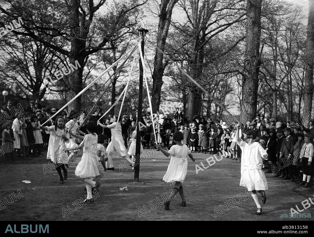 Entitled: "Playgrounds, May Day. May pole dance." Maypole dancing is a form of folk dance from Germany, England, and Sweden. The most popular maypole dance consists of dancers that perform circle dances around a tall, garland-festooned pole (originally a live tree).The dancers move in a circle, each holding a colored ribbon attached to a much smaller pole. As they move around the pole, the dancers intertwine their ribbons either in a web around the pole or to plait it to the pole, itself. To unravel the ribbons, the dancers retrace their steps. Historians believe the first maypole dance originated as part of Germanic pagan fertility rituals. While dancers usually perform this dance in the spring on May 1 or May Day, those in Sweden perform it during their midsummer celebrations. Photographed by Harris & Ewing, 1924.