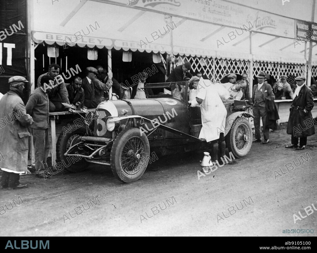 Le Mans 1927 Old Number 7 3 litre Bentley at the pits being refilled by Dr J D Benjafield while R A Clarke kneeling and W O Bentley next to him and Sammy Davis in crash helmet standing.