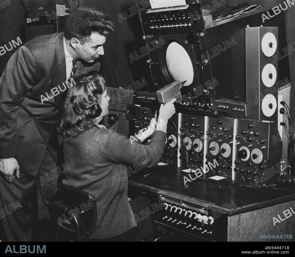New Device Aids Plane Landing - Mrs. Phyllis Barnes points a Volscan light gun at the "blip" of an incoming jet plane on radar scope in demonstration of new electronic method of controlling planes at an air base. Watching demonstration at Fort Dawes here today is Benjamin F. Greene, Jr., director of the project developed by U.S. Airplane's "blip" with a yellow square of light called a tracking gate which follows its course as the plane nears the air base. December 07, 1953. (Photo by AP Wirephoto).