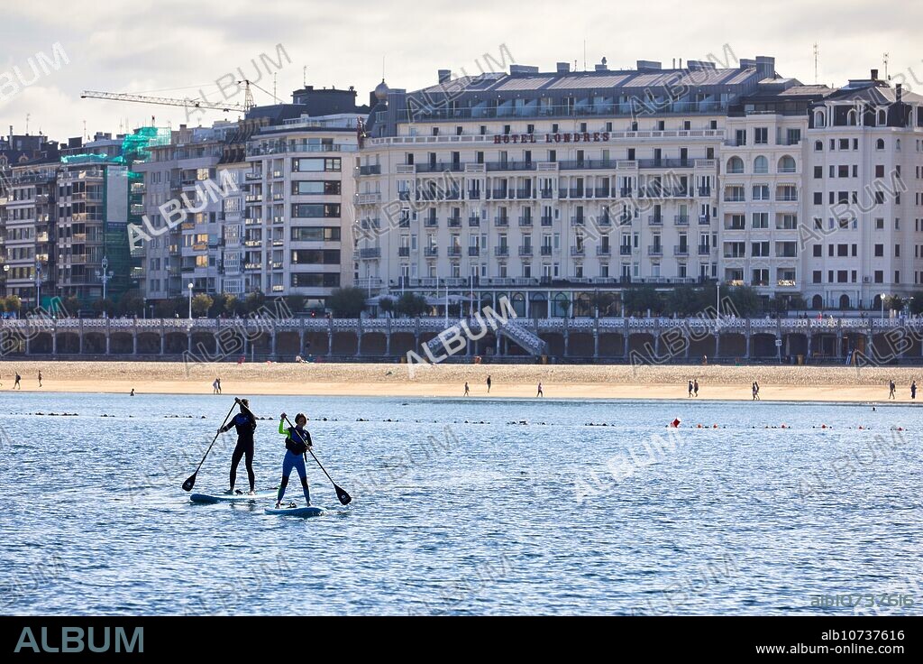 Pareja de turistas practicando paddle surf en la Bahia de La Concha, SUP, Stand Up Paddle, Detrás Hotel Londres, Donostia, San Sebastian, Pais Vasco, España.