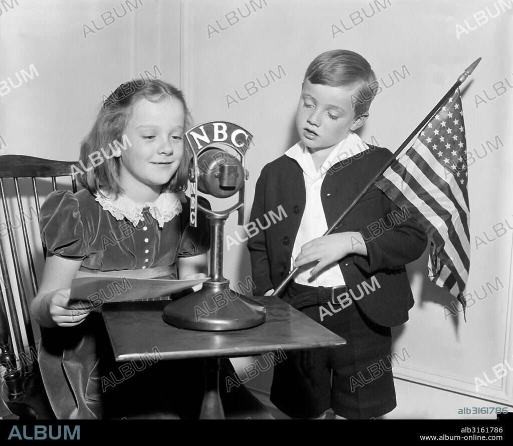United States: c. 1938. Two children with an American flag and a script do a patriotic broadcast on NBC radio.