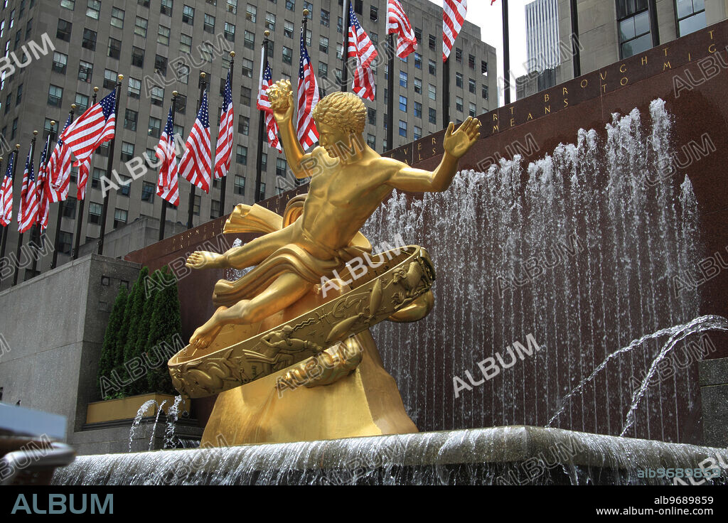The statue of Prometheus made by Paul Manship and it's water fountain in the Rockefeller Center Ice Skating Ring on a 4th of July, behind and above .U.S. flags fly high in front of the NBC building.. New York, N.Y. USA. July 4th, 2013.