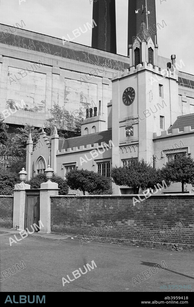 Trinity Hospital, Greenwich, London, c1945-c1965, was founded in 1613 by the Earl of Northampton, is overshadowed by Greenwich power station. The building has been much altered, and the main front (seen here), similar to a church in style, may date from the early 19th century.