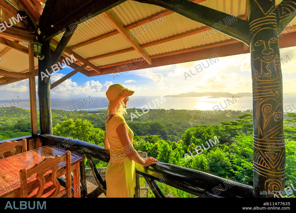 Tourist woman in yellow dress looks towards Praslin Island and La Digue panorama from highest point of island at sunset, La Digue, Seychelles, Indian Ocean, Africa.