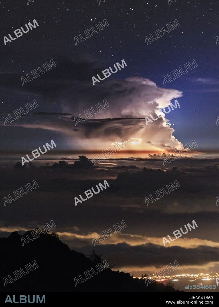 A thunderstorm rages against starry backdrop, seen from Haleakala volcanic summit on the island of Maui, Hawaii. Lightning appears in the supercell with the shelf cloud under it.