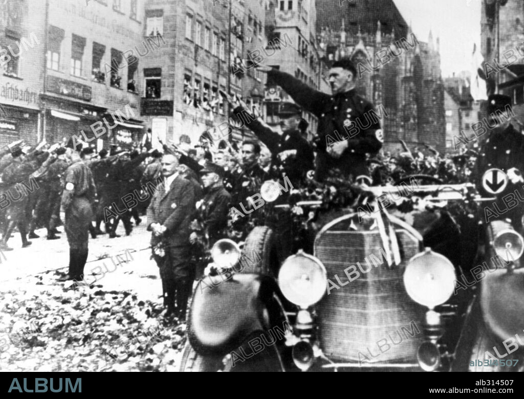 Hitler wearing an early nazi uniform and an swastika armband, reviews the marching members of the growing party on the occasion of the 1927 rally.