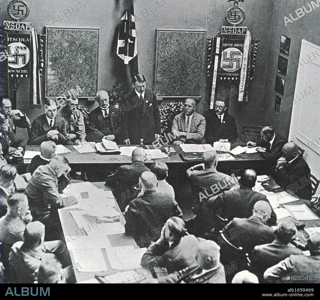 Hitler in Munich adressing a meeting of the NSDAP in 1925. Third to the left of Hitler is Alfred Rosenberg, on the right are Gregor Strasser and Heinrich Himmler. Far right by the door is Julius Streicher.