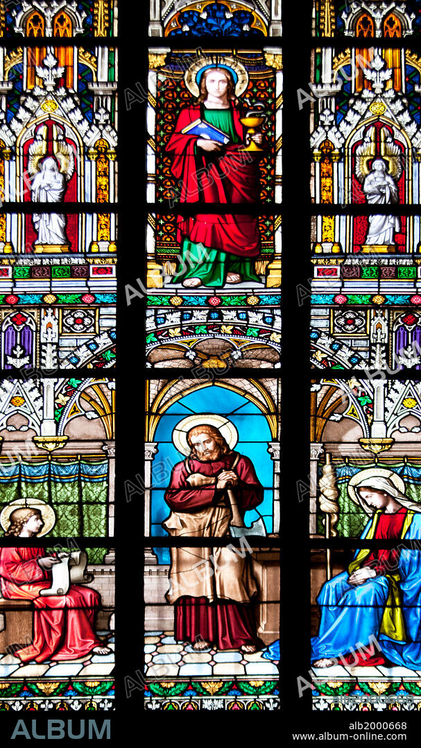 Prague, St. Vitus Cathedral, Stained Glass Window, St. Joanna, Jesus Holding a Hatchet. Part of a Stained Glass window depicting, vertically, two religious scenes, one on top of the other. The upper scene shows St Joanna holding a book and a golden grail; the lower scene shows Jesus holding a Hatchet, flanked by two seated female saints, one of which is holding a parchment.