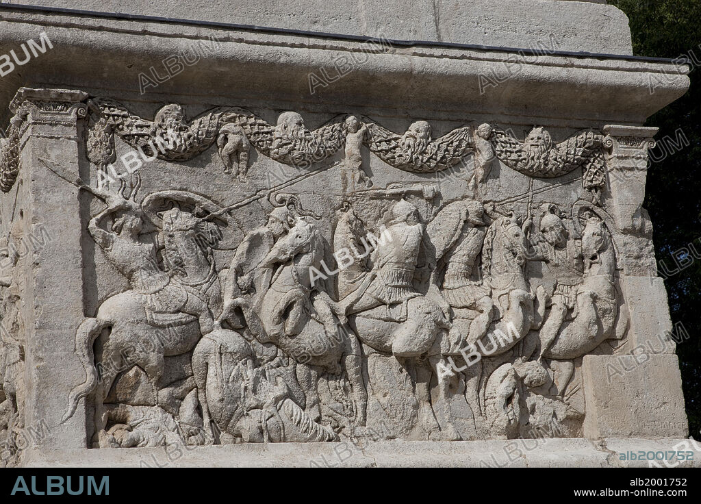 The Cenotaph of the Julii dates from c. 20 BC. It is one of the best preserved in the Roman world. It bears and inscription and has an unusual tiered form. Its pedestal is carved with historical and mythical reliefs. Seen here is the north face, with a relief depicting a cavalry battle, representing a scene from the Iliad. Above the pedestal is a quadrifrons arch, topped with a structure resembling a round temple or tholos, and in it statues of the dedicatees.