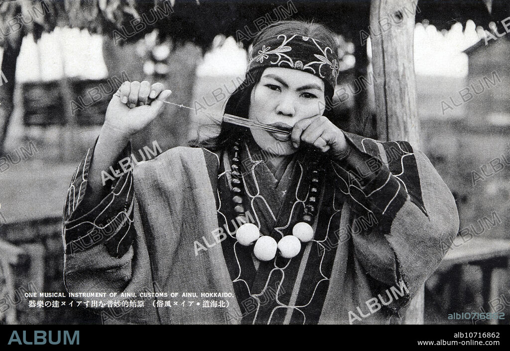 [ 1920s Japan - Ainu Woman ] An Ainu woman playing the Mukkuri (, a Jews harp). The Mukkuri is a traditional Ainu musical instrument played by women. It is made of carefully cut bamboo with two strings. 20th century vintage postcard.