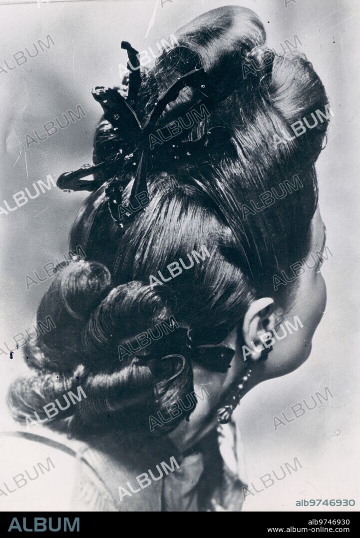 1946. En la Imagen, original peinado de fantasía compuesto de los Grandes Rizos en la frente y el pelo muy tirante de los Lados. El cuello por detrás Va cubierto de un grupo de Rizos Sujetos por una cinta de Terciopelo, que Hace juego con la de la Nuca.