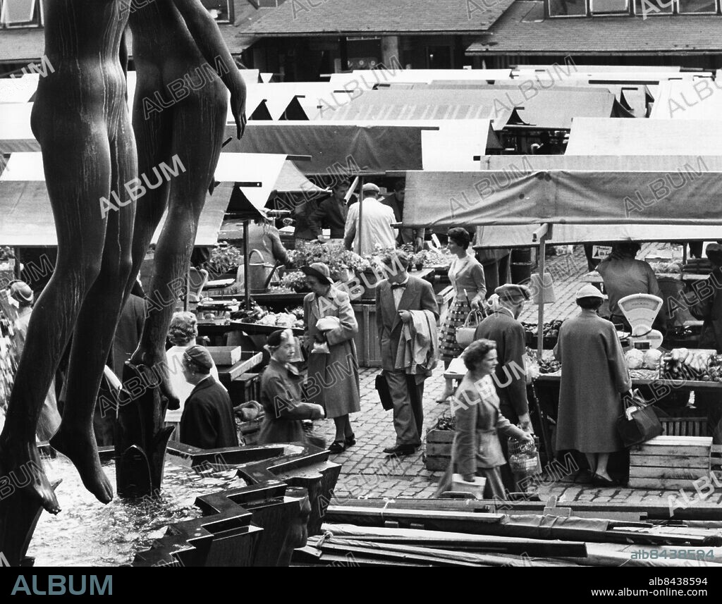 ARKIV STOCKHOLM 19580724.. Några människor rör sig bland stånden på ett torg med en fontän i förgrunden.. Foto: Ulf Stråhle / SVT / Kod: 5600. Reportage publ. i RiR 32/58 om torg- och saluhandel i Stockholm.. RiR sv/v 14574. Mapp: Torg- och saluhandel, juli 1958 R 63.
