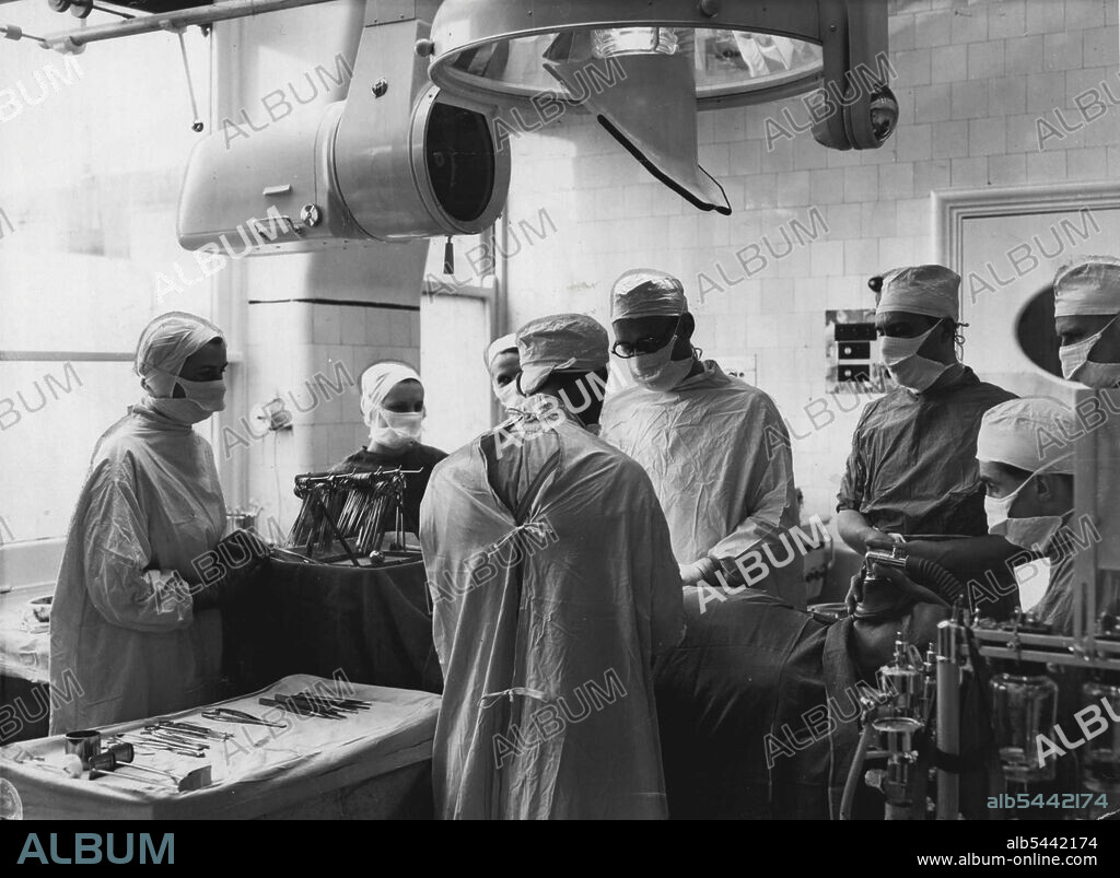 Televising An Operation -- The Television of the Appendicitis operation in progress. On the left Can be seen the C.P.S. Emitron Camera and on the right the "Scilytio" light with the mirror set at an angle of 45 degrees to reflect the operation into the camera. Under the camera can be seen a handle with which the surgeon can rotate the whole unit though 60 degrees. July 11, 1951.