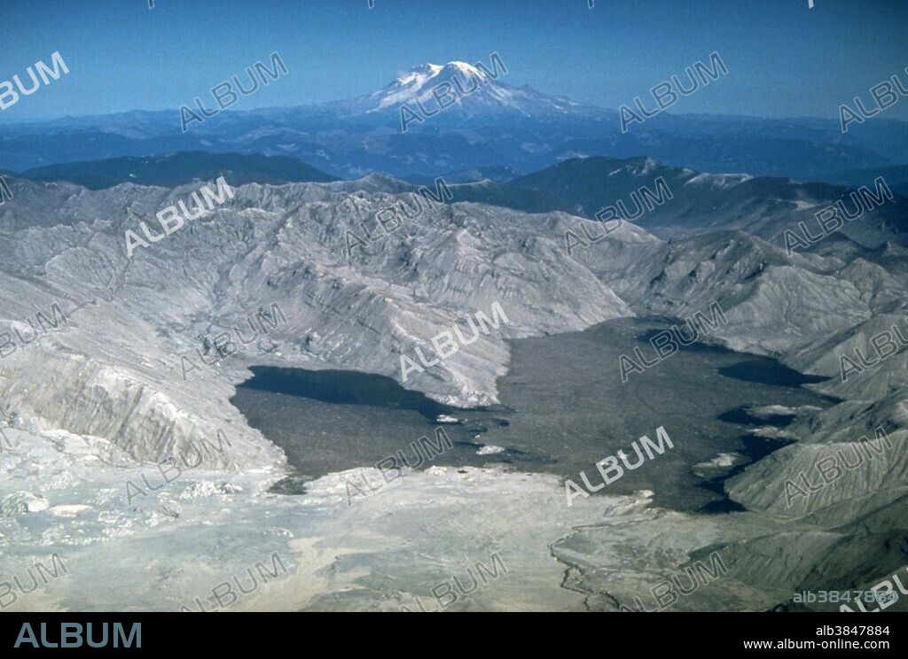 Spirit Lake, once surrounded by lush forest, is within the area devastated by the blast of Mount St. Helens on May 18, 1980. Remnants of the forest float on the surface of the lake. Another Cascade volcano, Mount Rainier (14,410 feet [4,392 meters]), is in the distance. The view is from the south. October 4, 1980.