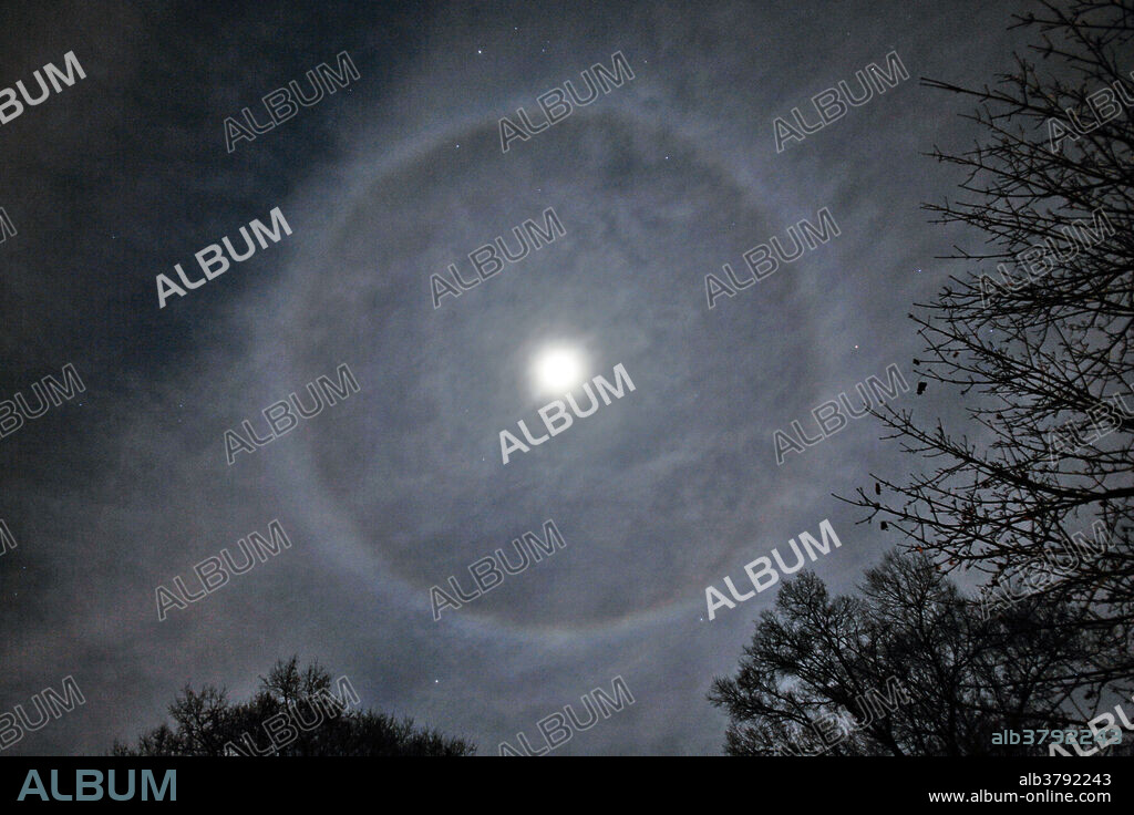 This is a 'ring around the moon' or lunar halo. Overexposed in the centre of the frame, is the Moon. Lunar halos are caused by moonlight being refracted by cirro-stratus clouds. These thin clouds are located very high in the atmosphere, and are composed of ice crystals. They bend light at a 22 degree angle, which creates a halo that is 44 degrees in diameter.