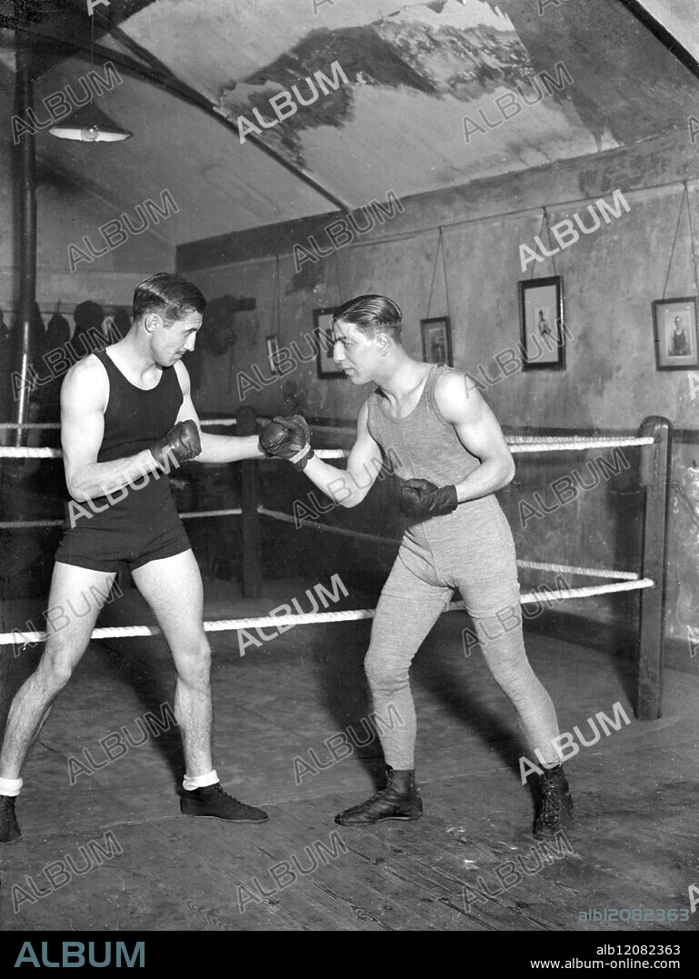BOXING PEER IN TRAINING FOR FIGHT WITH POLICE-CONSTABLE. : Lord Knebworth, the 23 year old heir of the Earl of Lytton, who has already distinguished himself as a boxer of the welter-weight class, is in strict training for his four-round contest with Police Constable Bone of the Metropolitan Police at Ilford on April 2. He is training under Mr Alan Lambert with Alf Mancini, the professional boxer, as his sparring partner. Photo Shows: Lord Knebworth (left) sparring with Alf Mancini at his training quarters. United Kingdom 1928.