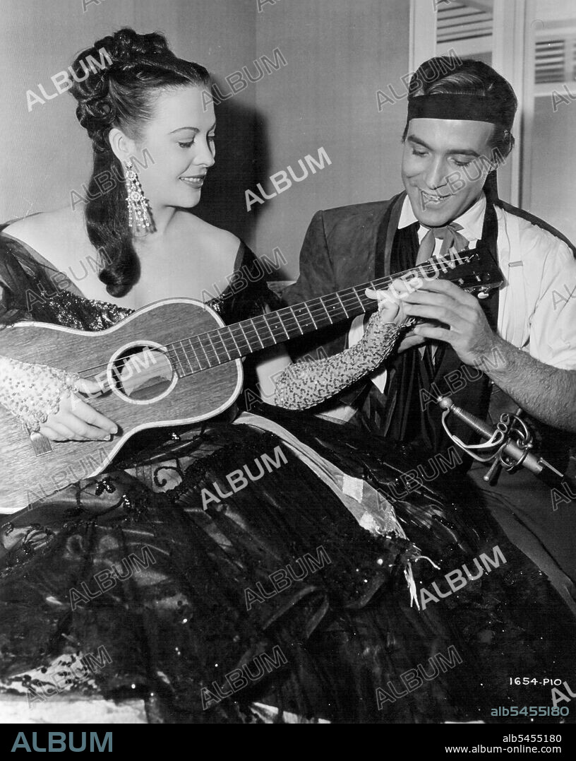 Don Renegade -- Six Lessons From Senor Montalban: Andrea King gets some expert instruction on guitar strumming from Ricardo Montalban between scenes in Universal International's "Don Renegade", a technicolor story of Early California. And Montalban isn't stringing her along - he plays a guitar with the touch of a professional. September 15, 1952.