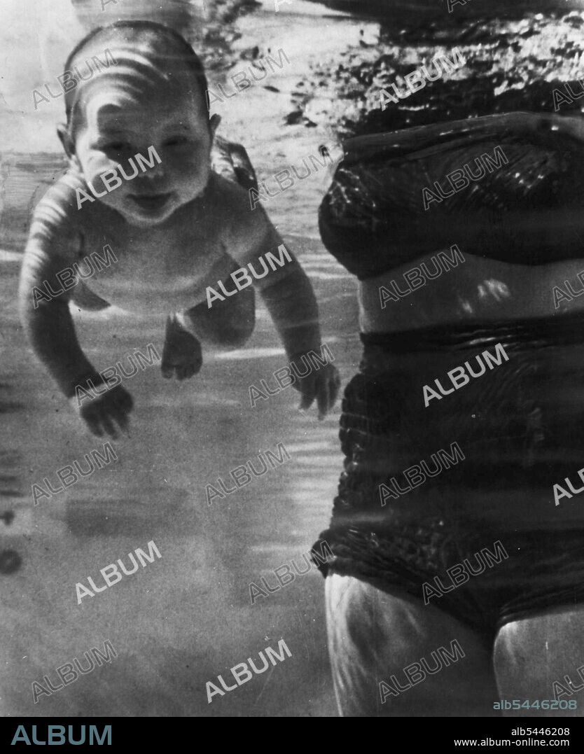 Precocious Swimmers -- Julie Sheldon, two months old moves like this under water for distances up to 10 feet, says her grandmother and swimming coach, Mrs. Jen Loven, standing at right. The baby flails her arms when left unsupported in the water, says Mrs. Loven, instinctively holding her breach as she strikes out and showing no fear of the water. Picture made from an underwater window of the pool. January 2, 1954. (Photo by AP Wirephoto).