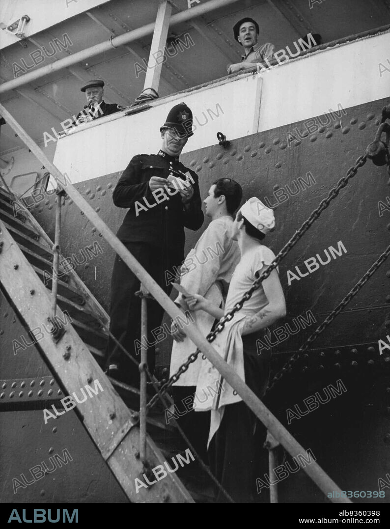 Inspecting Passes At The Beaverbrae -- A policeman on duty at the Canadian ship Beaverbrae inspecting the passes of Canadian seamen (non strikers) as they go aboard the vessel in Royal Victoria Dock, London to-day (Tuesday), first day of the State of Emergency regulations at London docks. The Beaverbrae and another Canadian ship, the Argomont, have been involved in a Canadian seamen's strike. Because London dockers refuse to work on them and the dock employers say the Canadian ships must be worked before any otehrs more than 10,000 men are now idle in the port of London and 112 ships held up, causing the King - on the Privy Council's advice  - to proclaim the State of Emergency. Troops are now working at the docks. July 12, 1949. (Photo by Reuterphoto).