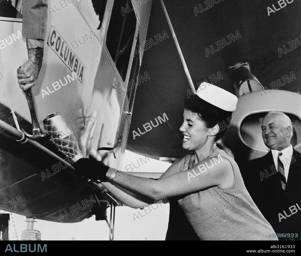 Akron, Ohio: August 27, 1963. Miss America, Jacquelyn Mayer, gets a helping hand hammer from the pilot as she christens the gondola of Goodyear's new blimp, Columbia. Goodyear Chairman E. J. Thomas watches the ceremony.