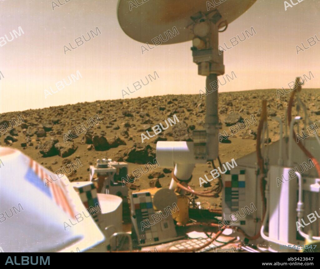 Viking 2 image of Mars Utopian Plain, September 3, 1976. The boulder-strewn field of red rocks reaches to the horizon nearly two miles from the Viking 2 spacecraft. Scientists believe the colours of the Martian surface and sky in this image represent their true colours. Fine particles of red dust have settled on spacecraft surfaces. The salmon colour of the sky is caused by dust particles suspended in the atmosphere. Colour calibration charts for the cameras are mounted at three locations on the spacecraft. Note the blue star field and red stripes of the US flag. The circular structure at top is the high-gain antenna, pointed toward Earth. Viking 2 landed some 4600 miles from its twin, Viking 1, which touched down on July 20, 1976.