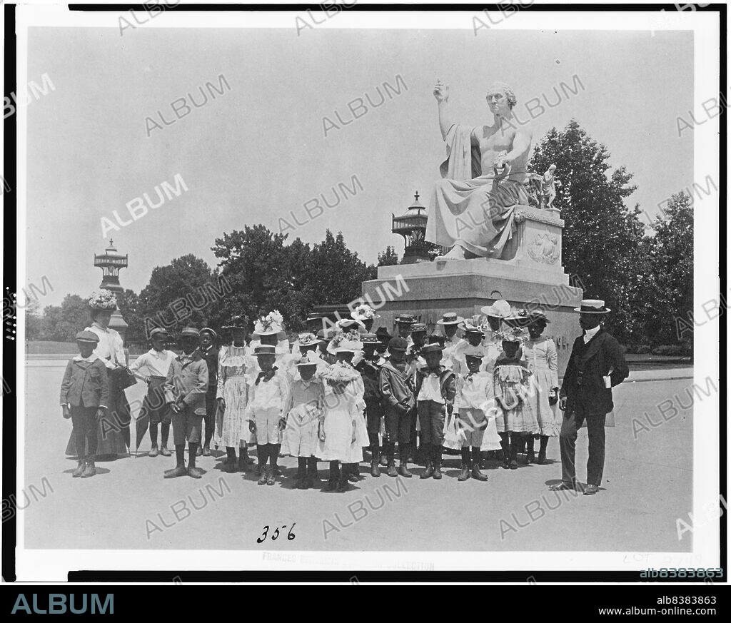 FRANCES BENJAMIN JOHNSTON. Group of school children in front of statue of George Washington, Washington, D.C., (1899?). [African American children on a school trip, with the 'Enthroned Washington' sculpture by Horatio Greenough behind. George Washington is depicted as a Roman emperor in a toga].
