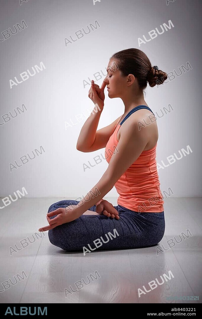 Beautiful sporty fit yogini woman practices pranayama breath control exercise in yoga asana Padmasana, lotus pose with Vishnu mudra in studio.